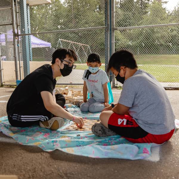 A student playing a board game with two kids at City Camp