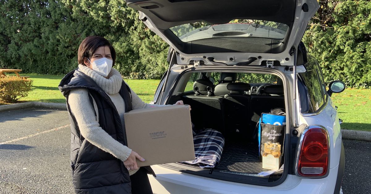 WCK volunteer Colleen wearing a mask and holding a WCK-stamped box full of frozen meals, about to load it into her car to deliver to the hospital.