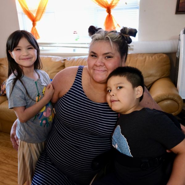 Mom and two kids in their living room all hugging and smiling at the camera. 