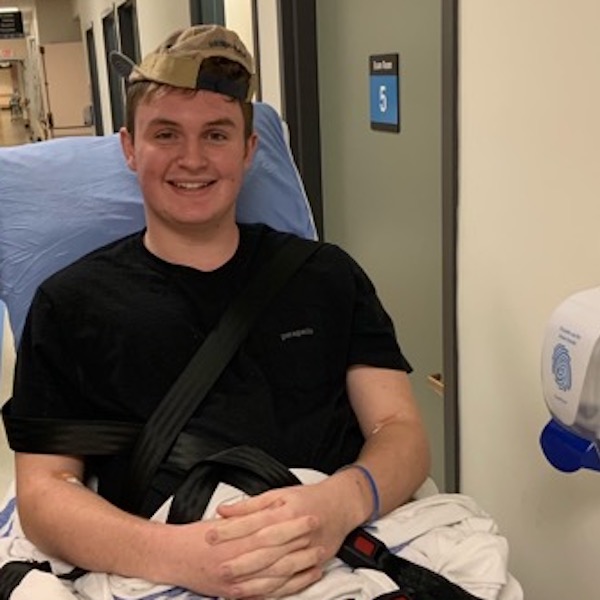 Kevin sitting in a hospital bed wearing his rally cap and smiling at the camera