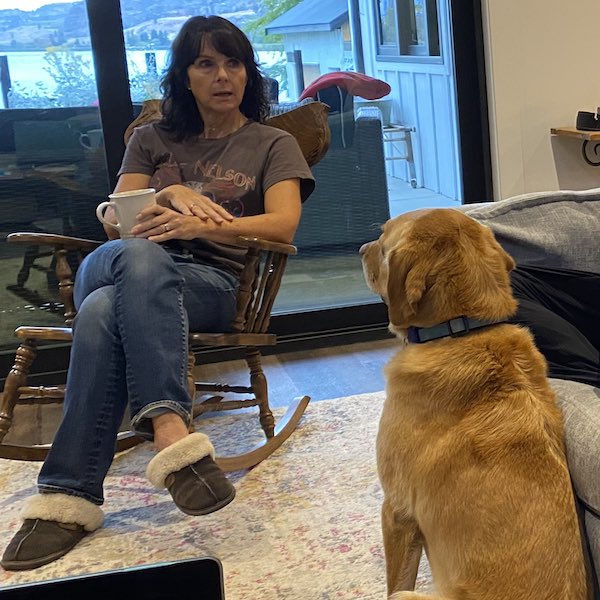 Leslie sitting in an armchair taking part in a team discussion, with her pet labrador looking on
