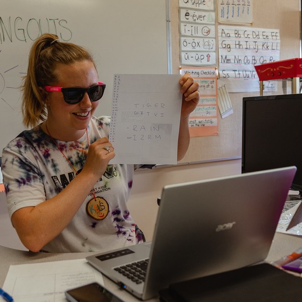 Kelsey wearing sunglasses and holding up a spy code to the screen, running a virtual session at City Camp