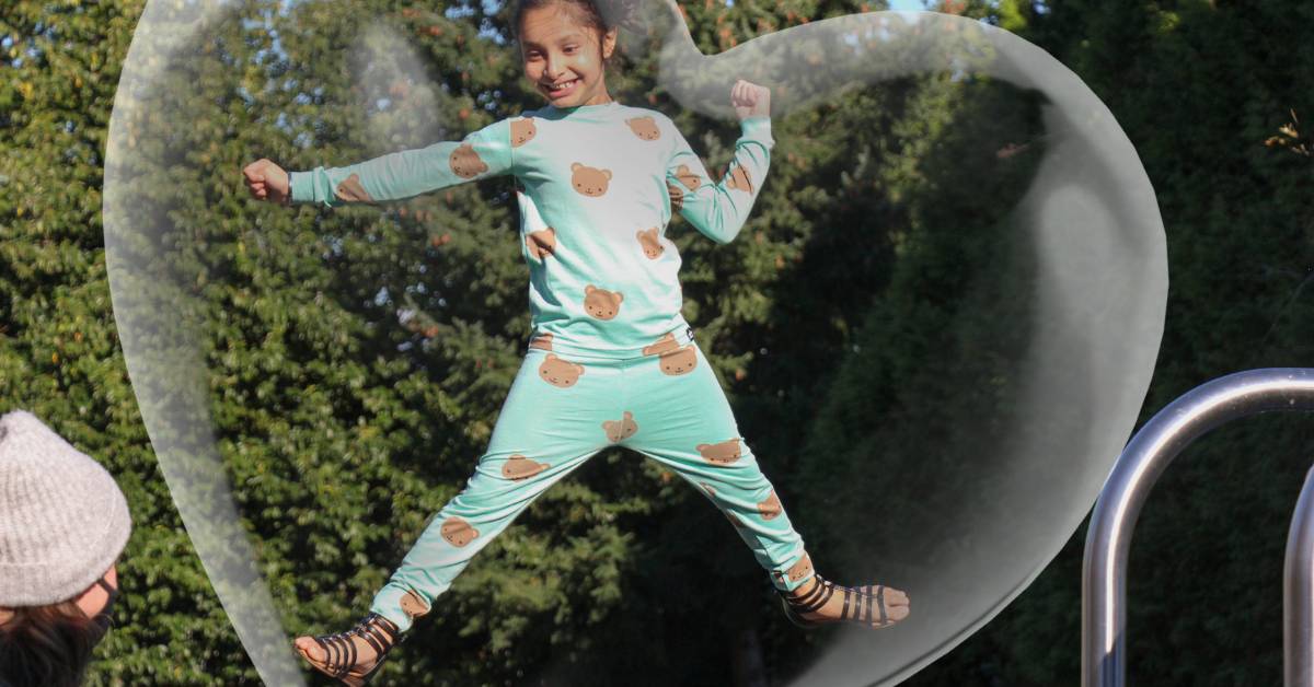 A young girl wearing PJs bouncing on her trampoline and smiling. There's a heart bubble effect surrounding her.