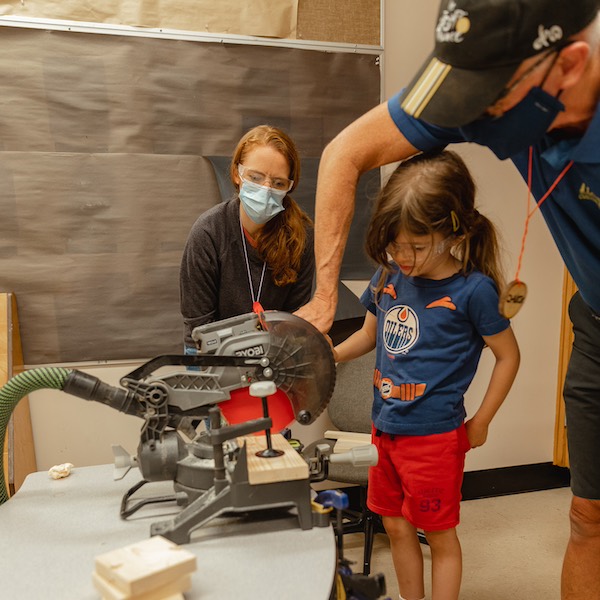 A young girl at City Camp being helped by Chuck to use a power tool.