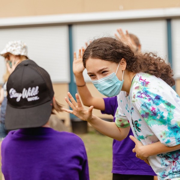 A WCK volunteer high fiving and smiling at a kid at City Camp. The volunteer is wearing a mask.