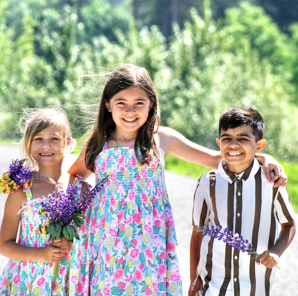 Ezra is holding some lavender and smiling at the camera. His sister has her arm around him, and is standing next to their other sister, who is holding a lavender bouquet.