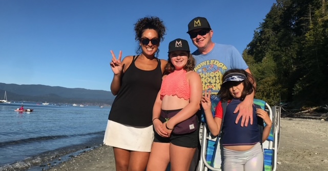 Mina with her family, standing in a sunny spot and smiling for the camera.