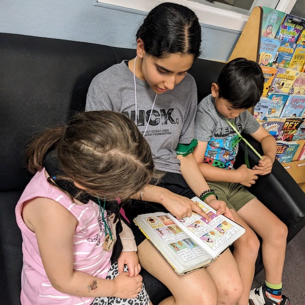 A WCK volunteer sitting on a couch with two kids reading a story to them