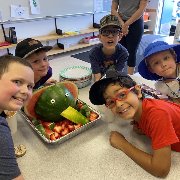 Five kids standing around a table with a watermelon snack made to look like an elephant with googly eyes and a watermelon trunk!